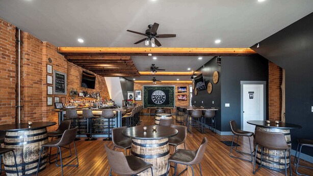 A bar area with wooden barrels as tables, bar stools, and a counter with a menu. - Monmouth Loft 4 (Newport)