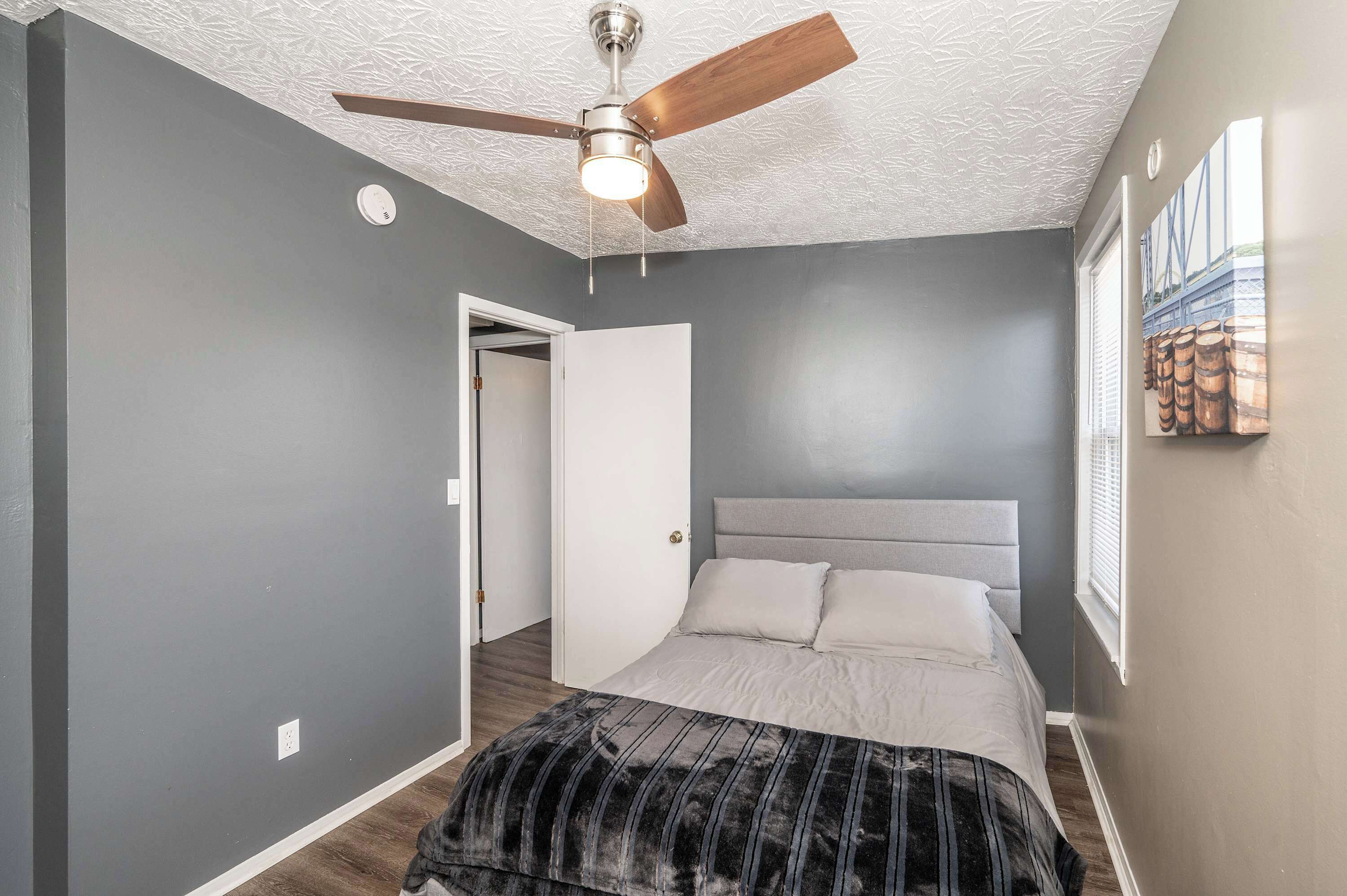 Un dormitorio con cama, ventilador de techo y puerta que da a otra habitación.