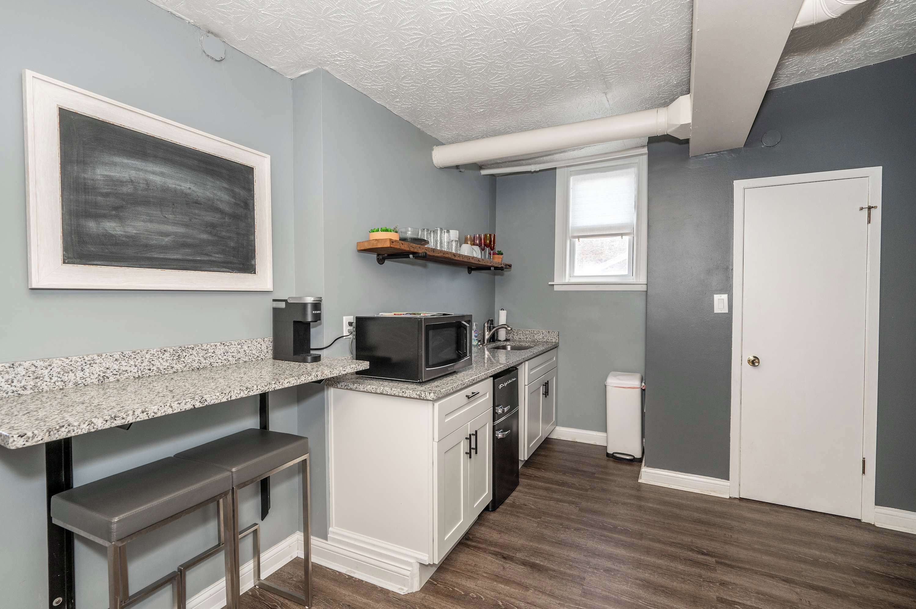 A kitchen with a granite countertop, white cabinets, a microwave, and a small bar area.