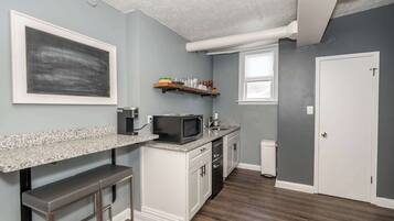 A kitchen with a granite countertop, white cabinets, a microwave, and a small bar area.