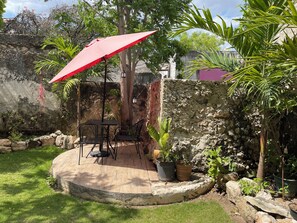 A patio area with a table and chairs, surrounded by potted plants and a stone wall. - Encantadora Suite, en la Mejor Zona de Paseo Montejo. En el Barrio Gastronómico (Mérida)