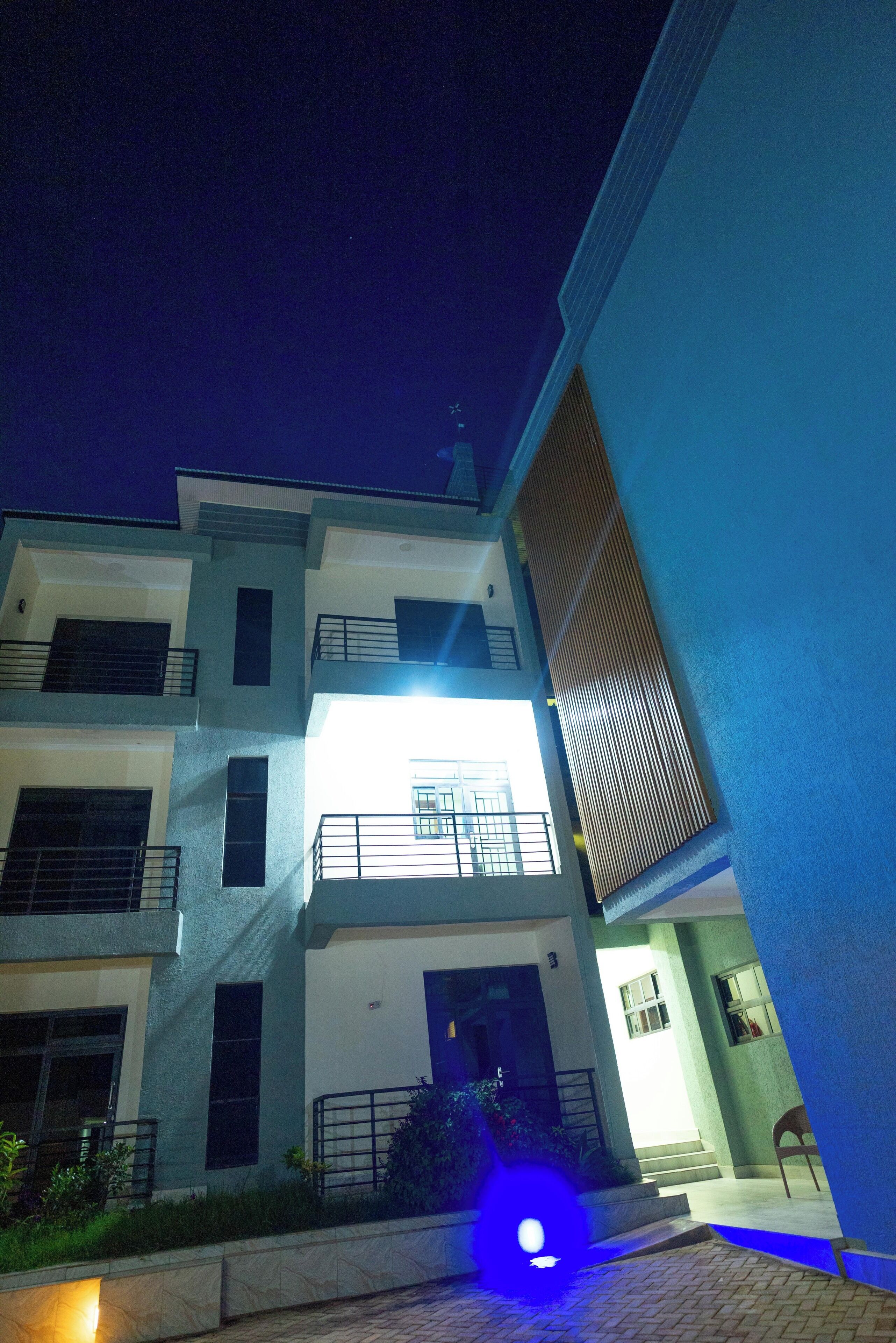 A multi-story building with balconies, a central entrance, and a well-lit facade.