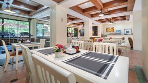 Un comedor con mesas y sillas blancas, un ventilador de techo y vistas al exterior.