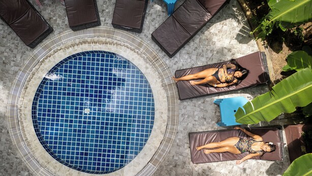Una piscina circular con borde de azulejos, rodeada de sillas de descanso y sombrillas.
