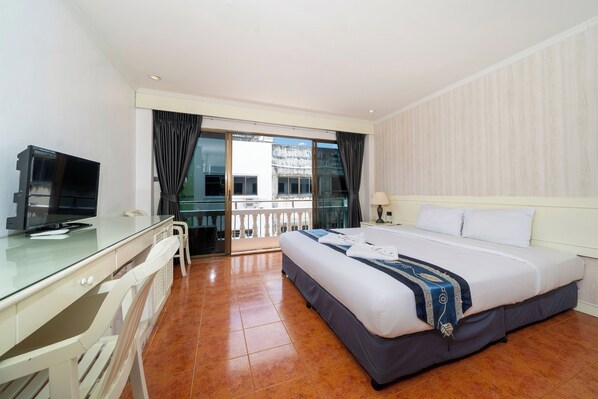 Habitación de hotel con cama, escritorio, televisión y balcón con vistas.