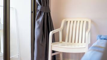 Una silla de plástico blanca junto a una ventana con cortina.