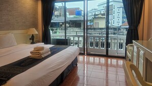 Habitación de hotel con una cama grande, una mesita de noche con lámpara, vista a edificios desde un balcón y piso de baldosas.
