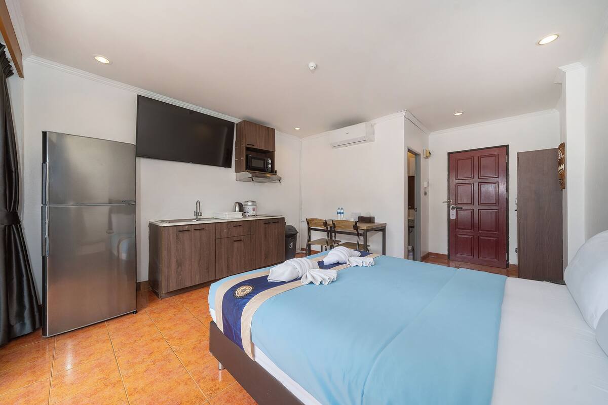 A hotel room with a bed, a kitchenette, a flat-screen TV, and a door.