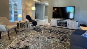 A hotel room with a large flat-screen TV, a ceiling fan, a seating area with two chairs and a sofa, and a patterned rug. - Melbourne, FL Home-Away From Home - Eau Gallie District  (Melbourne)