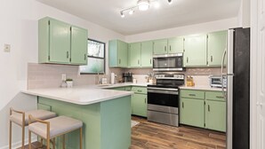 A modern kitchen with green cabinets, a stainless steel refrigerator, and a central island with bar stools. - Fire Pit/Golf Cart! 5 mins to Beach/DT! Fam Friendly! 4BR, 2 Kings! (Fernandina Beach)