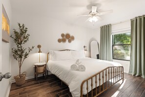 Un dormitorio con una cama de madera, una mesita de noche, un espejo en la pared y una ventana con cortinas.