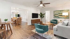 A spacious living room with a dining area, a ceiling fan, a flat-screen TV, and a large abstract painting on the wall. - Fire Pit/Golf Cart! 5 mins to Beach/DT! Fam Friendly! 4BR, 2 Kings! (Fernandina Beach)