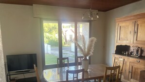 Een zithoek met een geruit vloertje, een tafel met stoelen, een vaas met gedroogd riet en een keuken met houten kastjes.