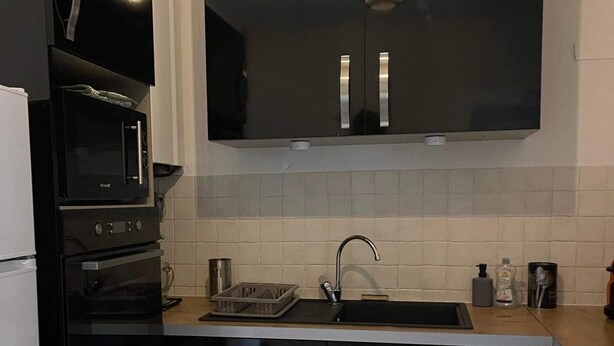 Een compacte keuken met zwarte kastjes, een roestvrijstalen spoelbak, een magnetron en een inbouwoven.