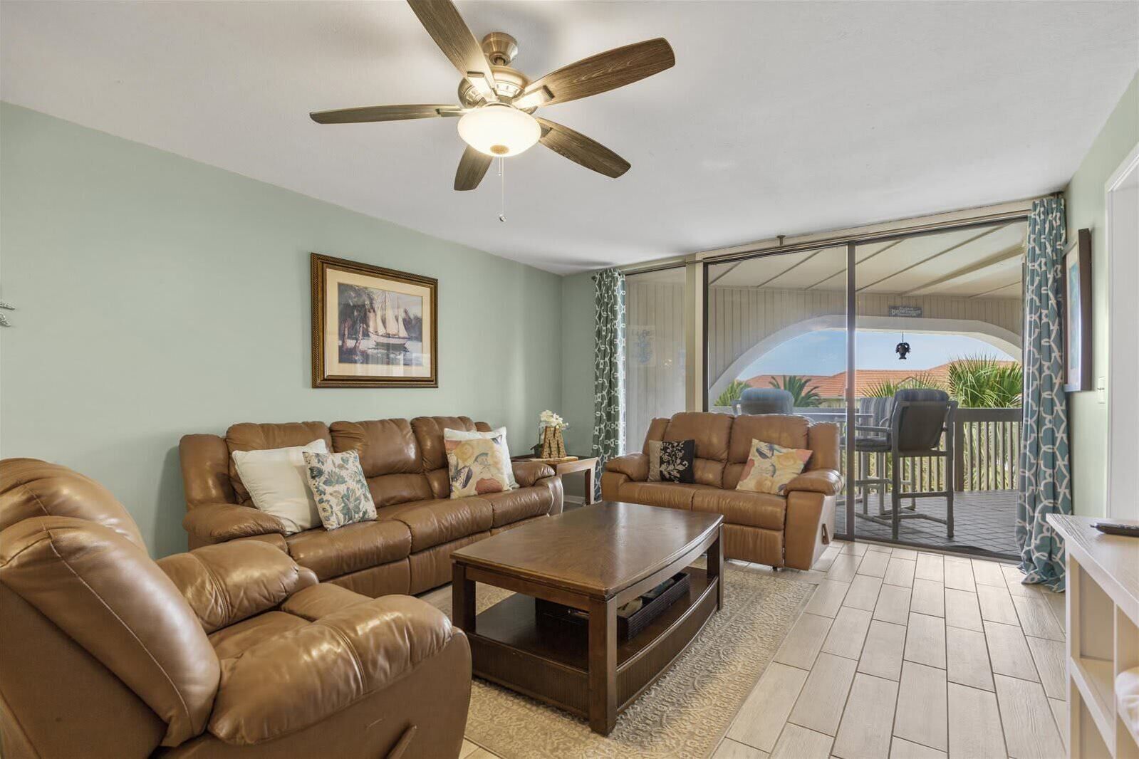 A living room with a brown leather sofa set, a wooden coffee table, and a ceiling fan.