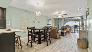 A spacious living area with a dining table, sofas, and a balcony with a view. - Ocean Hibiscus Oceanfront Resort (St. Augustine)