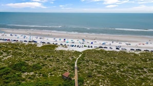 An aerial view of a beach with a wooden boardwalk leading to a small building, surrounded by dense green vegetation. - Ocean Hibiscus Oceanfront Resort (St. Augustine)