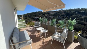 A balcony with a beige canopy, two wicker chairs, a small round table, and potted plants.