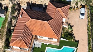 An aerial view of a large house with a swimming pool, multiple roof sections, and a driveway with a parked car.