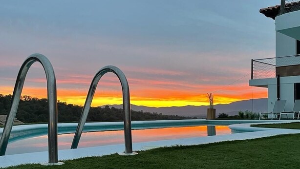 A swimming pool with two metal arches, a grassy area, and a building with a balcony in the background.