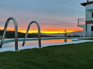 A swimming pool with two metal arches, a grassy area, and a building with a balcony in the background. - Spacious Villa with Private Pool & Gym – Only 20 min from Beach (Mas Altaba)