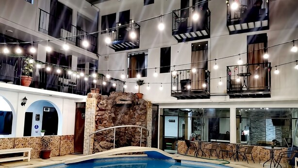 A multi-level indoor pool area with a stone wall, multiple balconies, and string lights. - Hotel San Isidro  (Pisco)