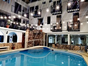 Uma área de piscina interior com vários níveis, parede de pedra, várias varandas e luzes de corda.