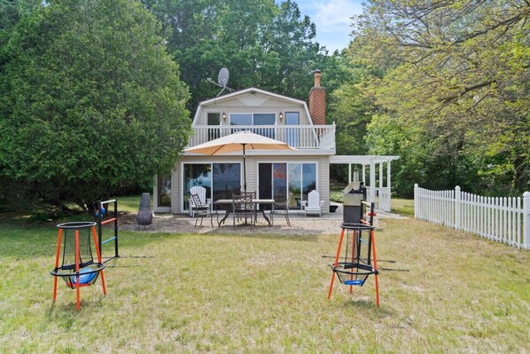 A two-story house with a patio area, a swing set, and a fenced yard. - Serenity Shores Hideaway - Great Beach & Peaceful! (Forester Township)