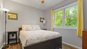 A bedroom with a bed, a nightstand, a floor lamp, a window with curtains, and a ceiling fan. - Hemlock Hideout - 3 Mins from DT Lex, Great Beach! (Lexington Township)