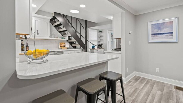 Une cuisine moderne avec un îlot central blanc, un escalier noir et un plancher en bois.