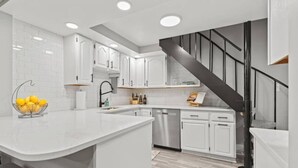 Une cuisine moderne avec des meubles blancs, un lave-vaisselle en acier inoxydable et un escalier noir.