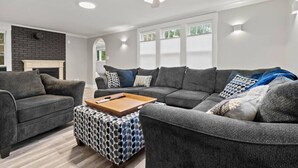 Un salon moderne avec un canapé gris, un pouf à motifs et une cheminée.