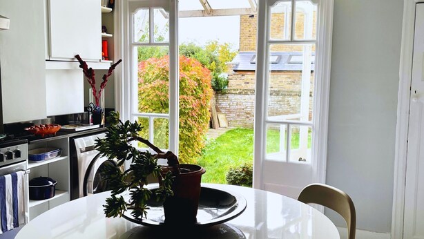 Une cuisine avec une table à manger, une plante en pot et une vue sur un jardin, visible à travers une porte vitrée.