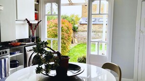 Une cuisine avec une table à manger, une plante en pot et une vue sur un jardin, visible à travers une porte vitrée.