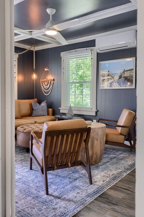 Une pièce chaleureuse avec un mur bleu foncé, une table basse ronde en bois, un canapé beige et une chaise en bois.