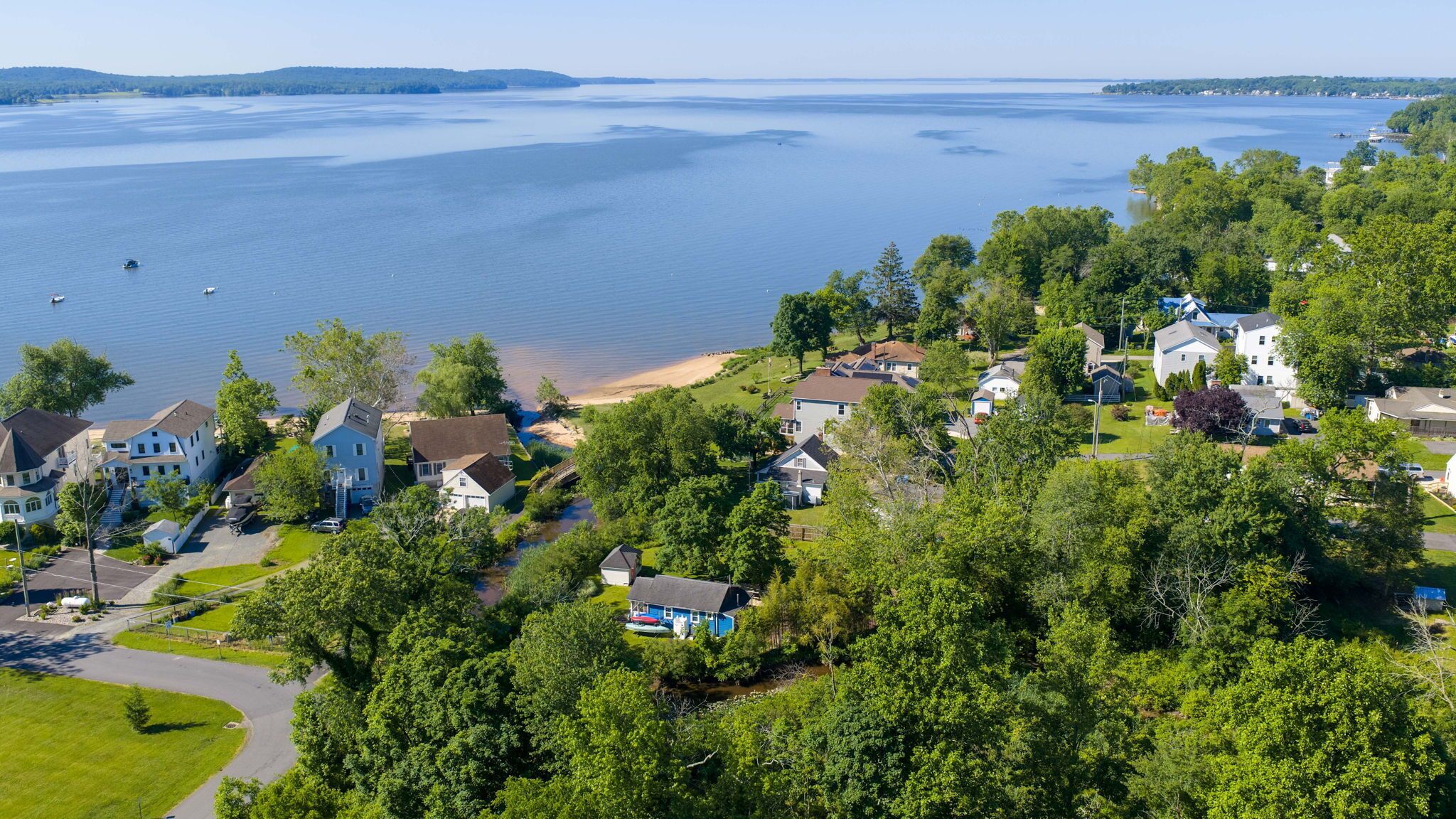 A residential area with houses near a large body of water, a beach, and dense greenery.