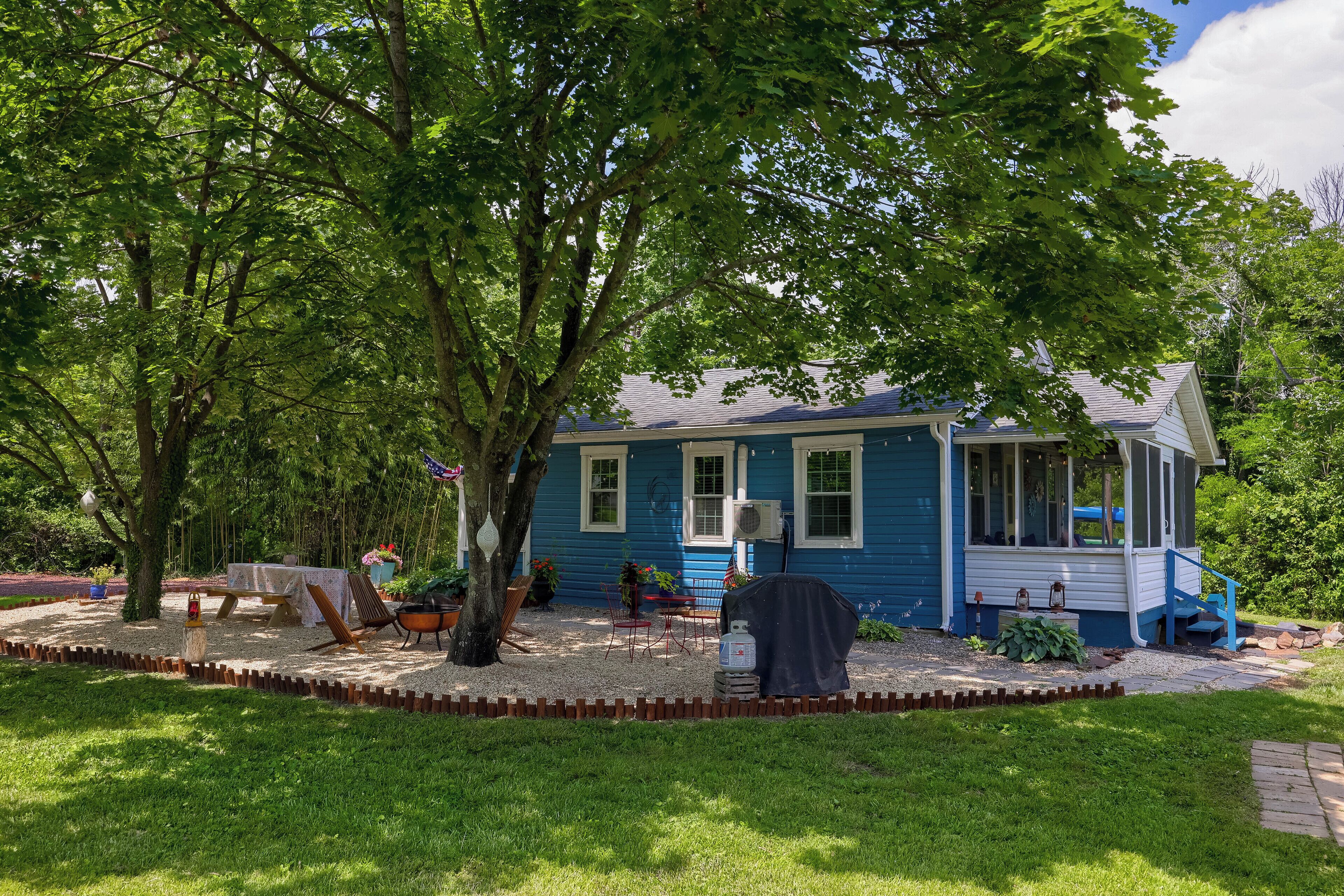 A blue house with a covered porch, surrounded by a well-maintained garden and trees.