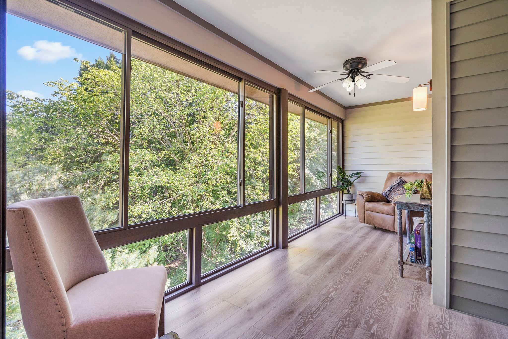 A spacious room with large windows, a ceiling fan, and a cozy seating area with a chair and a sofa.