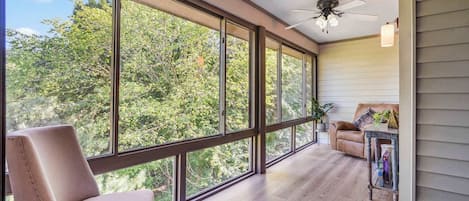 A spacious room with large windows, a ceiling fan, and a cozy seating area with a chair and a sofa.