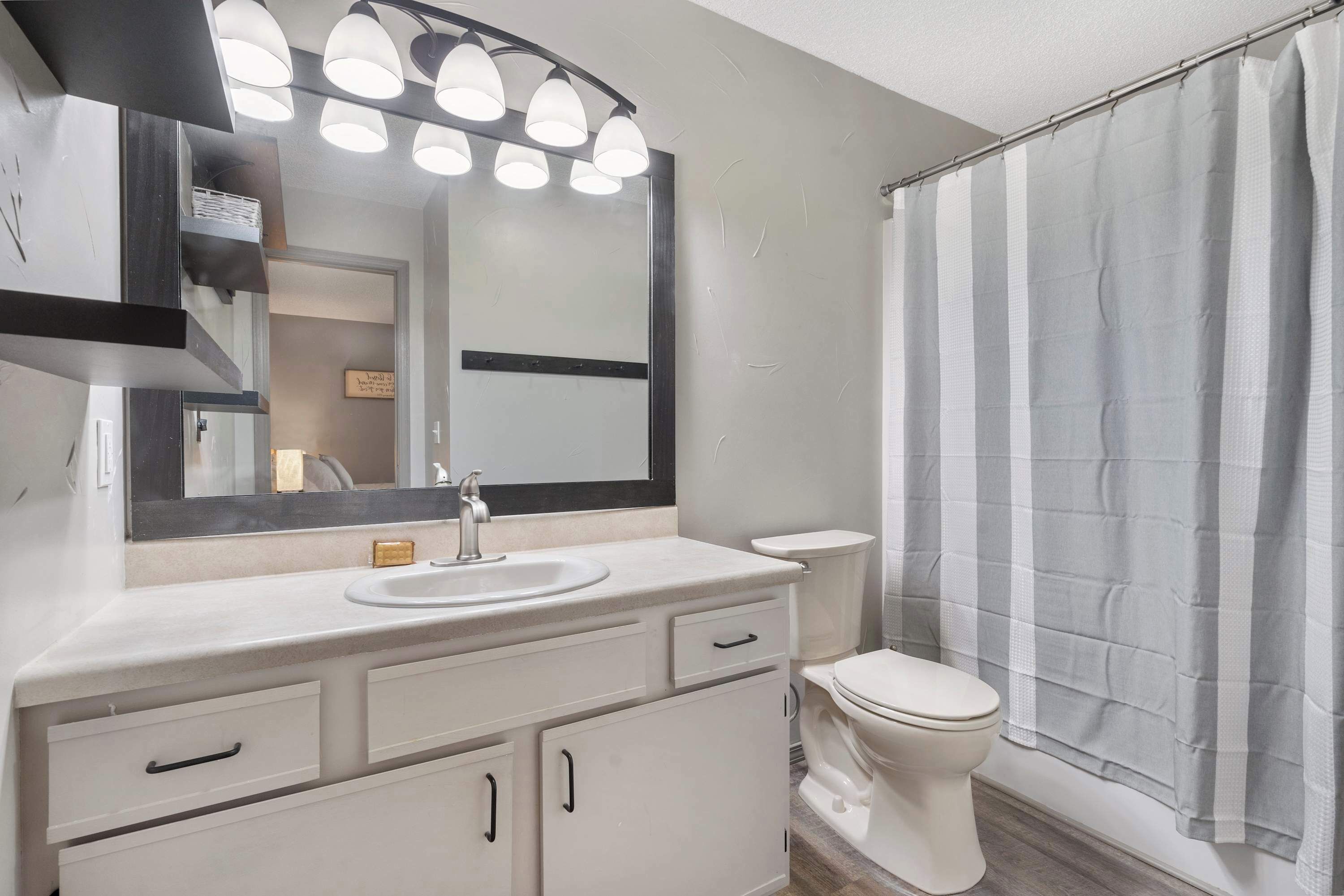 A modern bathroom with a white vanity, a large mirror, and a shower curtain.