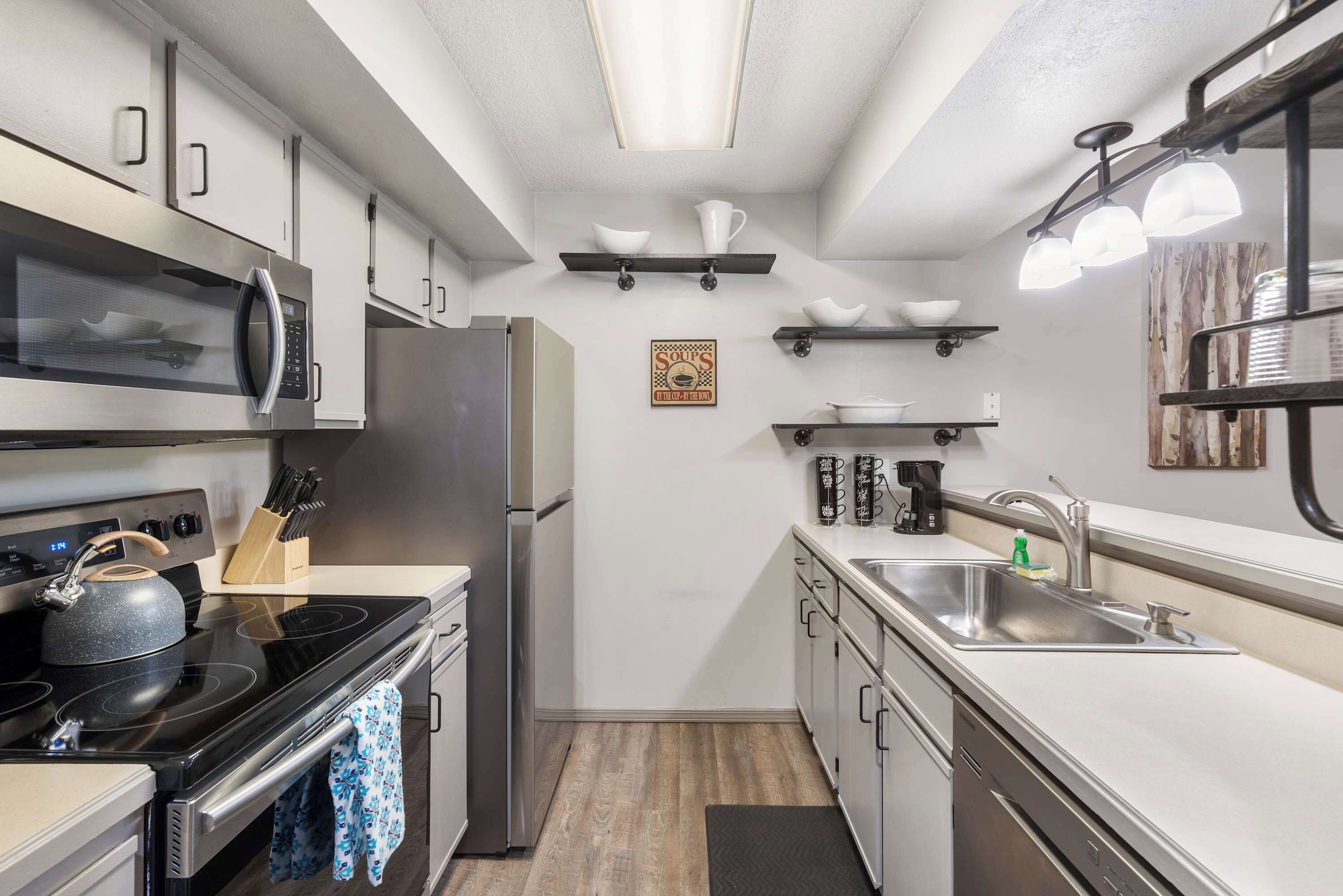 A modern kitchen with stainless steel appliances, a microwave, a kettle, and a sink.