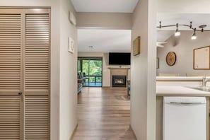 A hallway with a wooden door, a fireplace, a kitchen area with a dishwasher, and a large window. - Peek-a-boo Serenity Duo (Branson)