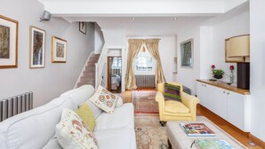 En rummelig stue med en hvid sofa, en gul lænestol og et sofabord. En trappe fører op til en etage.
