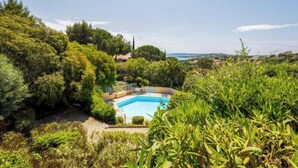 A pool surrounded by lush greenery and a clear view of the sea.