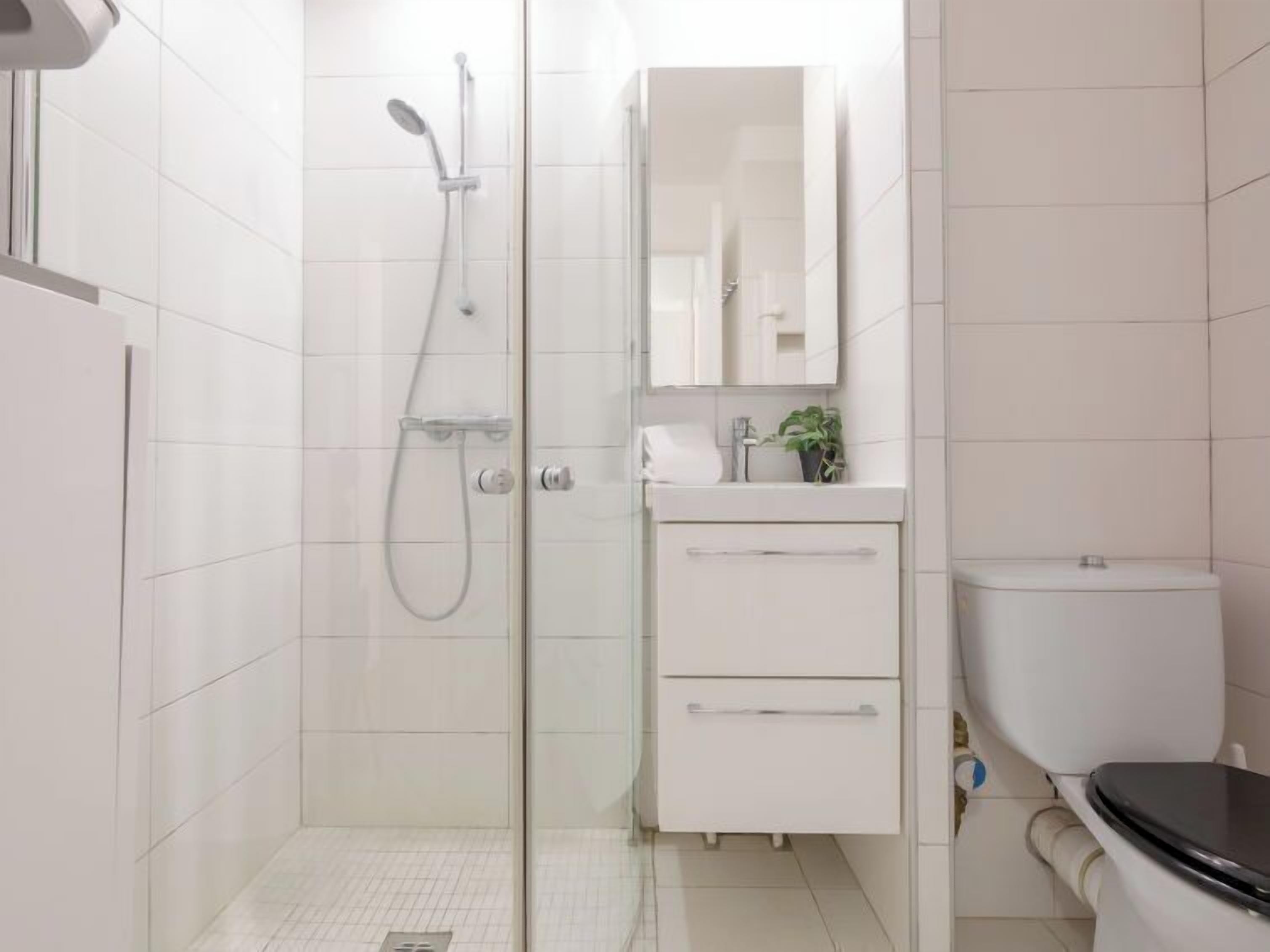 A modern bathroom with a glass shower enclosure, a white sink with a mirror above, and a toilet.