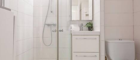 A modern bathroom with a glass shower enclosure, a white sink with a mirror above, and a toilet.