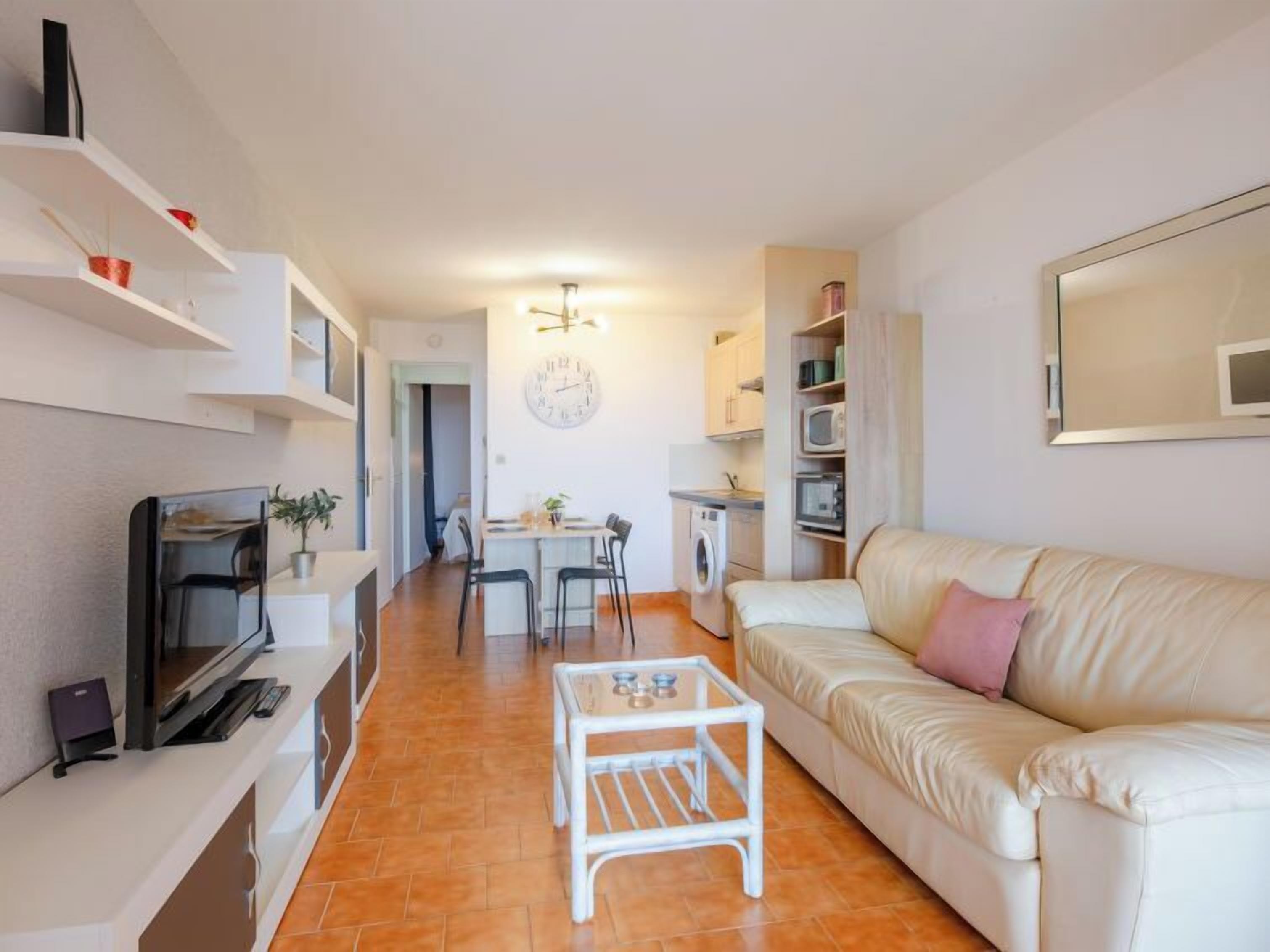 Ein kompakter Wohnbereich mit Sofa, Couchtisch, Fernseher, Essbereich und einer Küche.