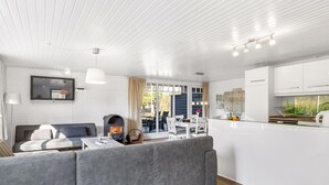 Een moderne woonkamer met een grijze bank, een open haard en een eethoek met een tafel en stoelen.