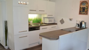 Een moderne keuken met witte kasten, een magnetron, een waterkoker en een klein eiland met een aanrecht.