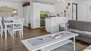 Een moderne woonkamer met een grijze bank, een witte salontafel en een eethoek met witte stoelen en een witte tafel.